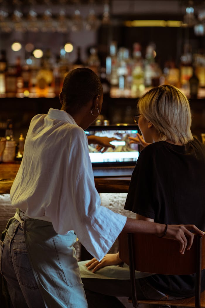 Mastering the First Impression: Your intriguing post title goes here Two women browsing a laptop together at a cozy café bar, seen from behind in a relaxed atmosphere.